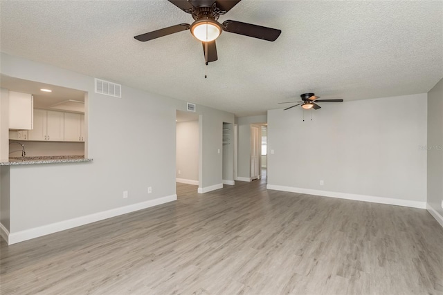 unfurnished living room with ceiling fan, a textured ceiling, and light hardwood / wood-style floors