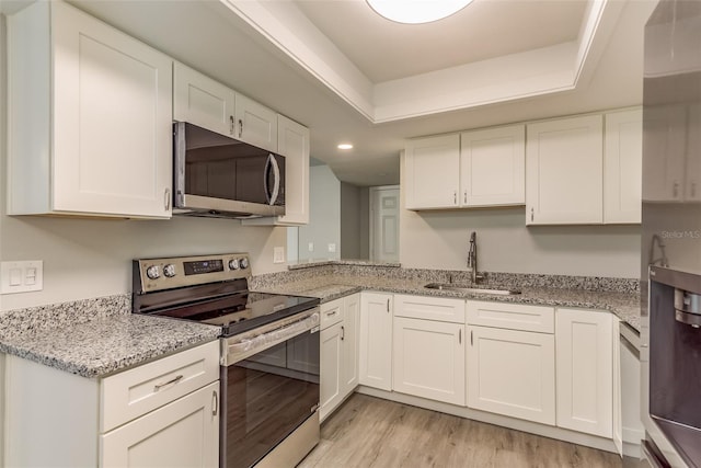 kitchen featuring appliances with stainless steel finishes, white cabinetry, light stone countertops, light wood-type flooring, and sink