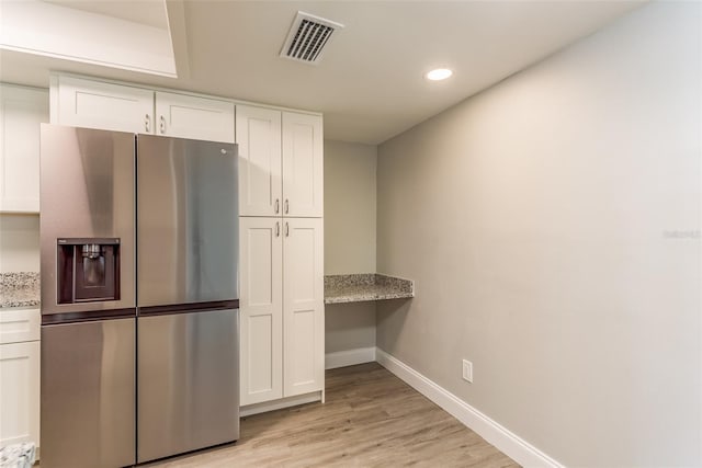 kitchen featuring stainless steel fridge, light stone countertops, and white cabinets