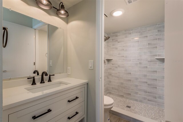 bathroom featuring a tile shower, vanity, and toilet