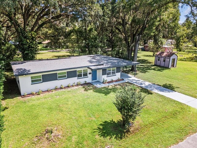 ranch-style house with a storage shed, a carport, driveway, an outdoor structure, and stucco siding