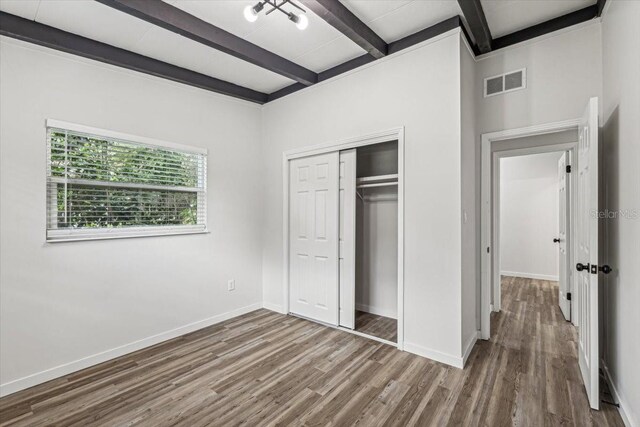 unfurnished bedroom featuring wood finished floors, a closet, beamed ceiling, baseboards, and visible vents