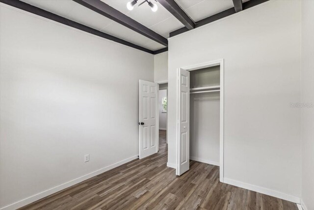 unfurnished bedroom featuring beamed ceiling, baseboards, wood finished floors, and a closet