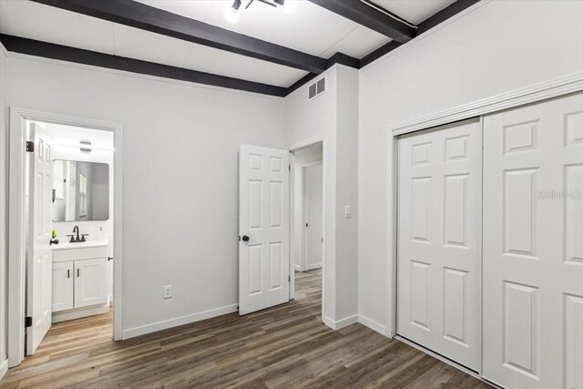 unfurnished bedroom with beamed ceiling, baseboards, wood finished floors, and visible vents