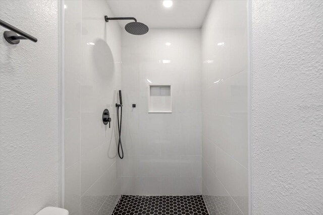 full bath with a textured wall and tiled shower