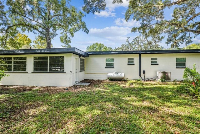 back of property featuring a lawn, central air condition unit, and concrete block siding