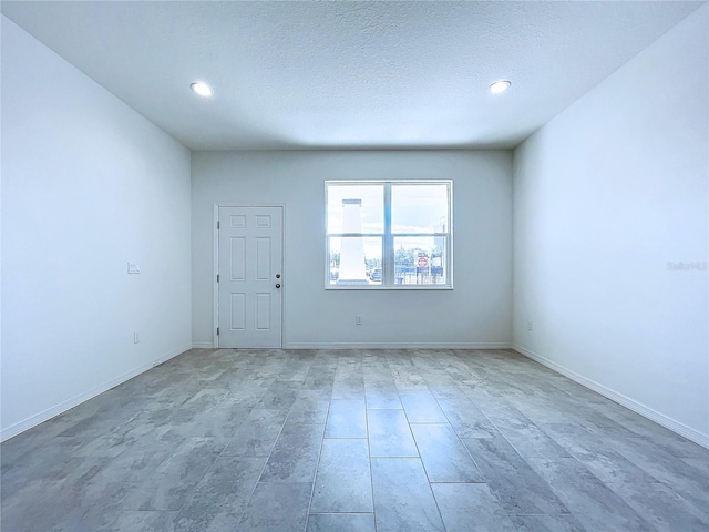 unfurnished room featuring a textured ceiling, recessed lighting, and baseboards