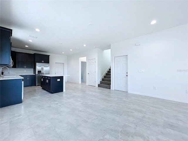 kitchen with stainless steel fridge with ice dispenser, a kitchen island, open floor plan, light countertops, and dark cabinetry