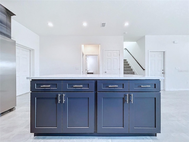 kitchen with light countertops, a kitchen island, stainless steel refrigerator, and visible vents