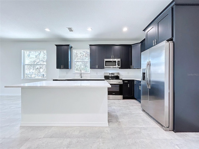 kitchen with dark cabinets, stainless steel appliances, a sink, visible vents, and a center island