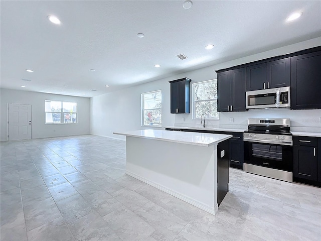 kitchen featuring a kitchen island, appliances with stainless steel finishes, open floor plan, light countertops, and dark cabinetry