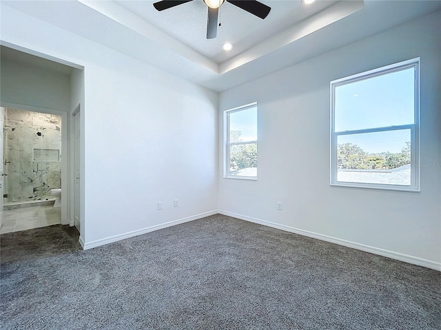 empty room featuring ceiling fan, recessed lighting, baseboards, dark colored carpet, and a raised ceiling