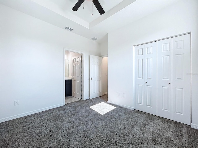 unfurnished bedroom featuring ceiling fan, dark colored carpet, connected bathroom, a tray ceiling, and a closet