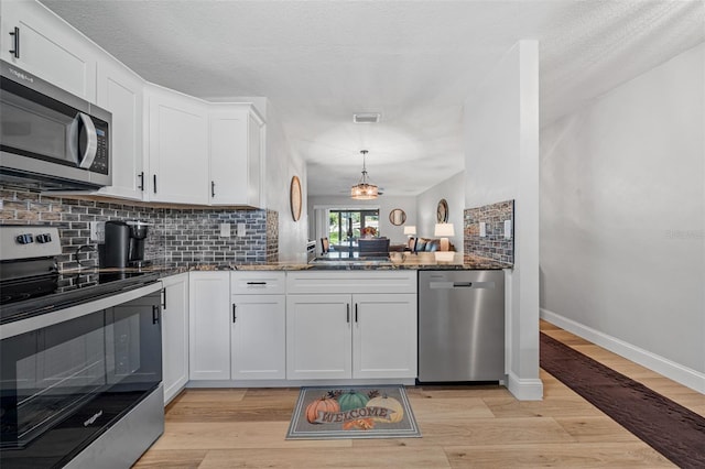 kitchen with backsplash, appliances with stainless steel finishes, dark stone counters, white cabinets, and light wood-type flooring