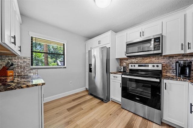 kitchen featuring white cabinets, stainless steel appliances, and dark stone counters