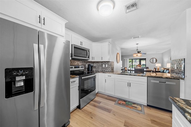 kitchen featuring backsplash, dark stone counters, appliances with stainless steel finishes, light hardwood / wood-style floors, and white cabinetry