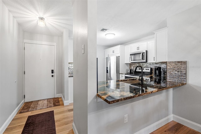 kitchen featuring sink, dark stone countertops, appliances with stainless steel finishes, tasteful backsplash, and white cabinetry