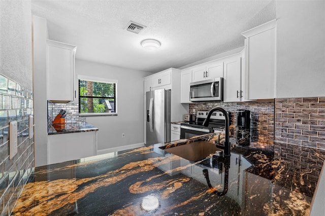 kitchen with white cabinets, decorative backsplash, dark stone countertops, a textured ceiling, and stainless steel appliances