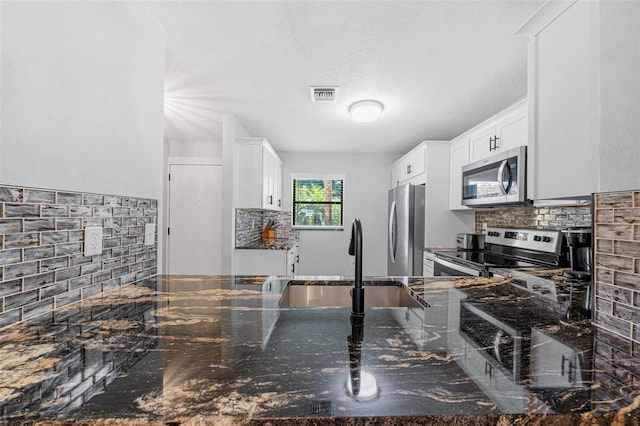 kitchen featuring backsplash, dark stone counters, stainless steel appliances, sink, and white cabinetry