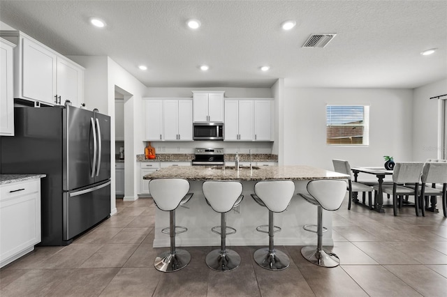 kitchen featuring an island with sink, white cabinetry, appliances with stainless steel finishes, and light stone countertops