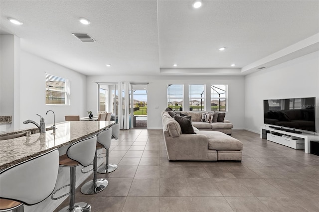 tiled living room with a textured ceiling, a tray ceiling, and sink