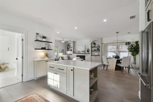 kitchen featuring high end refrigerator, ceiling fan with notable chandelier, pendant lighting, a center island, and light hardwood / wood-style floors