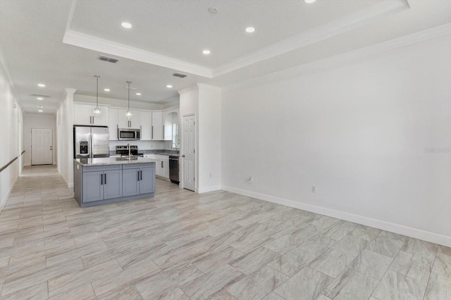 kitchen with a tray ceiling, a kitchen island with sink, white cabinetry, hanging light fixtures, and stainless steel appliances