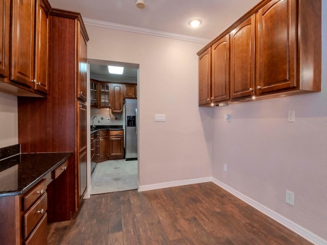 kitchen featuring stainless steel fridge, ornamental molding, sink, dark stone countertops, and dark hardwood / wood-style floors