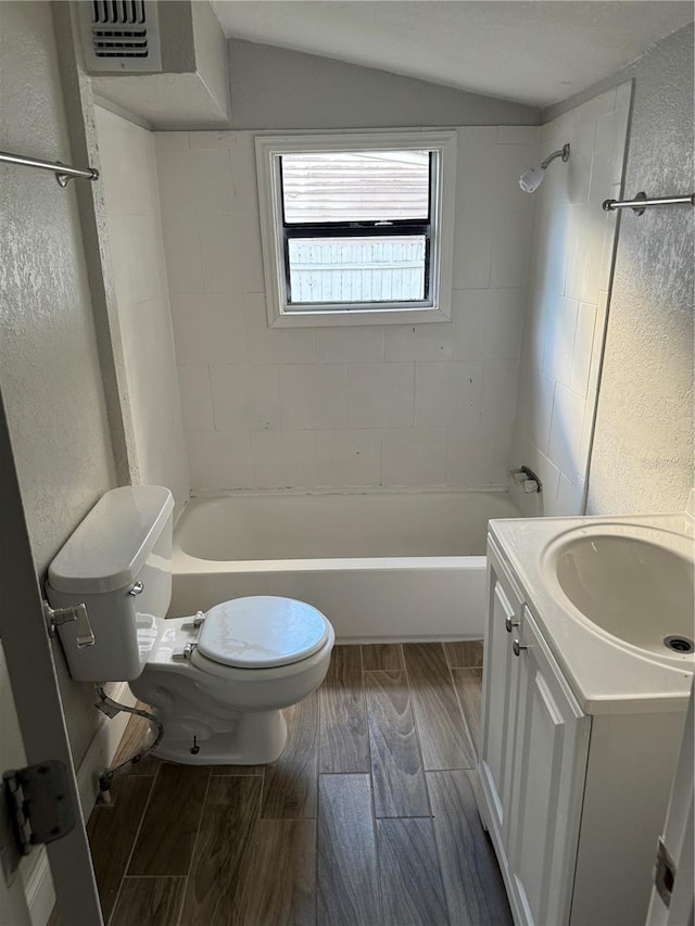 full bathroom with tiled shower / bath, vanity, lofted ceiling, and toilet