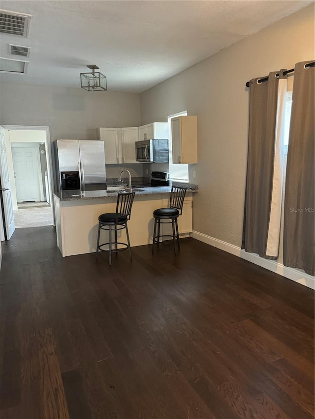 kitchen with a breakfast bar, kitchen peninsula, appliances with stainless steel finishes, and dark hardwood / wood-style floors