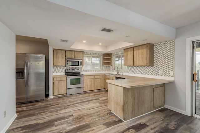 kitchen featuring appliances with stainless steel finishes, backsplash, kitchen peninsula, and dark hardwood / wood-style flooring