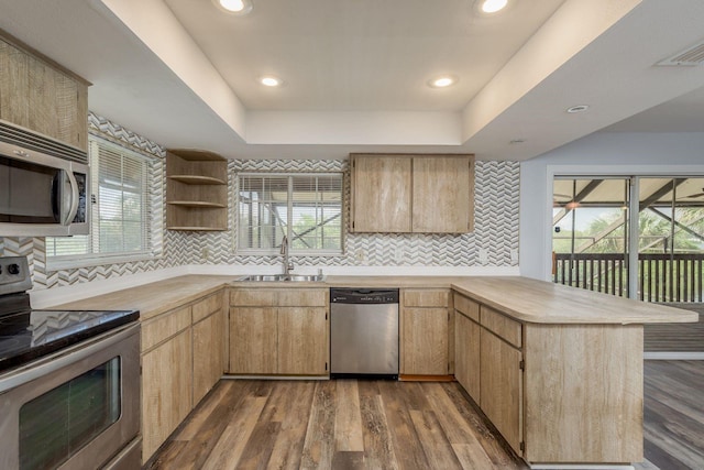 kitchen featuring a raised ceiling, sink, kitchen peninsula, dark wood-type flooring, and appliances with stainless steel finishes