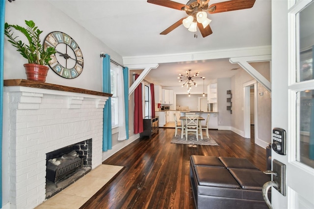 living room featuring a brick fireplace, ceiling fan with notable chandelier, and dark hardwood / wood-style flooring