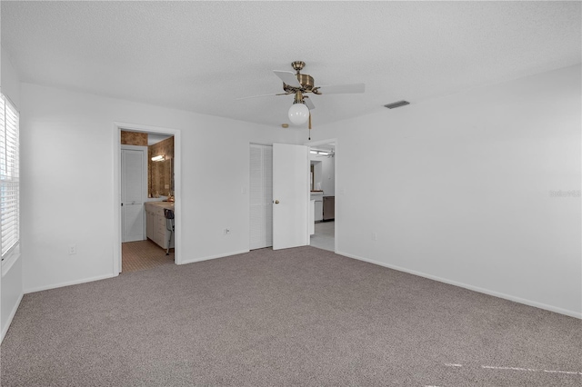 unfurnished bedroom with a textured ceiling, connected bathroom, light colored carpet, and ceiling fan