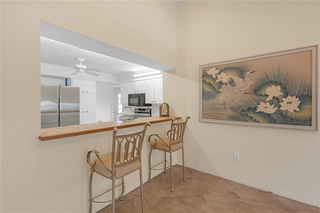 kitchen with appliances with stainless steel finishes, ceiling fan, a breakfast bar, white cabinetry, and kitchen peninsula