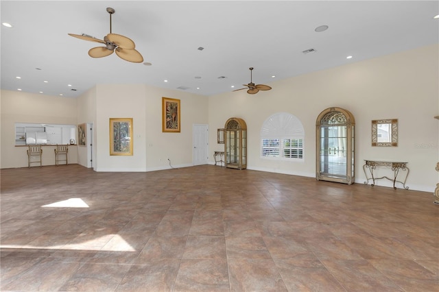 unfurnished living room with ceiling fan and a high ceiling