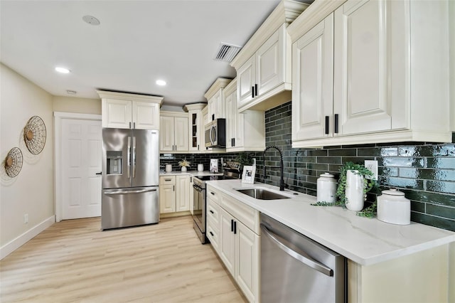 kitchen featuring a sink, stainless steel appliances, glass insert cabinets, tasteful backsplash, and light wood-type flooring