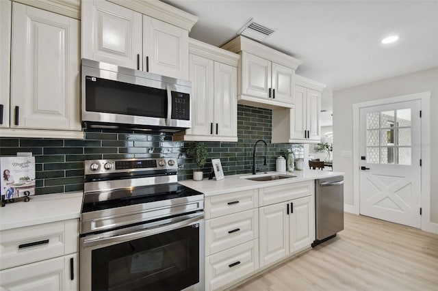 kitchen with light wood-style flooring, a sink, appliances with stainless steel finishes, light countertops, and decorative backsplash