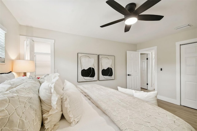 bedroom with a ceiling fan, wood finished floors, visible vents, and baseboards