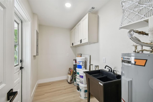 kitchen with light wood-type flooring, visible vents, electric water heater, white cabinets, and baseboards