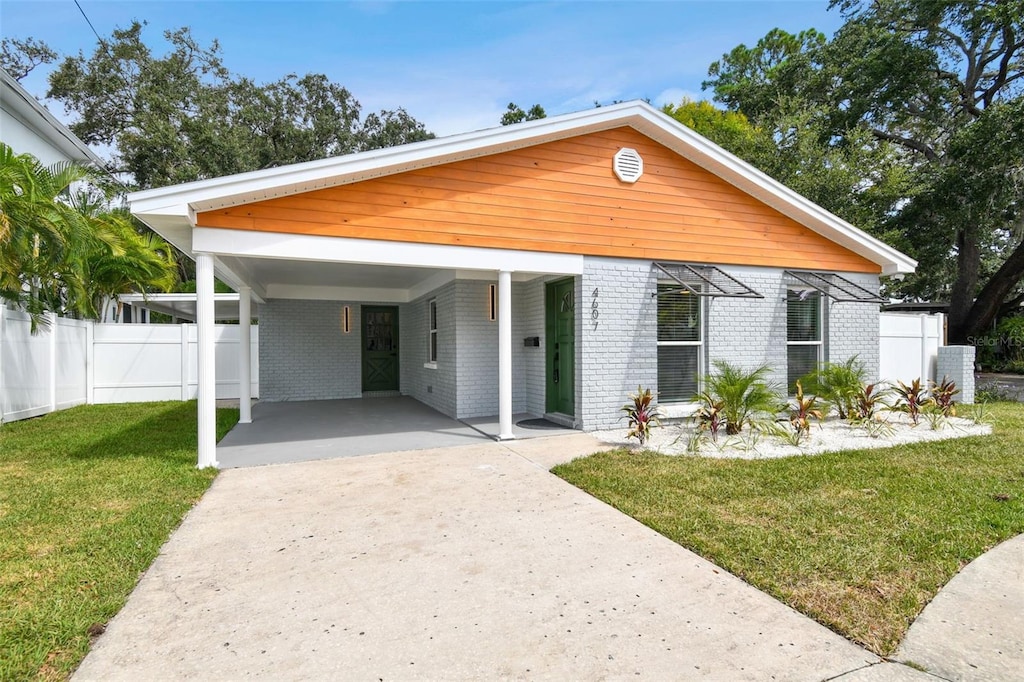 view of front of property with driveway, an attached carport, fence, a front yard, and brick siding