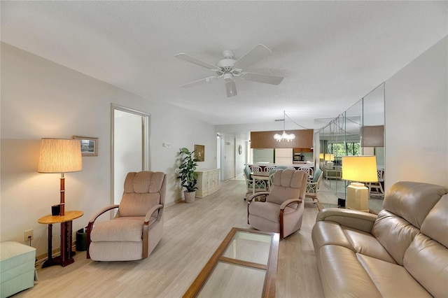 living room with light wood-type flooring, ceiling fan with notable chandelier, and a textured ceiling