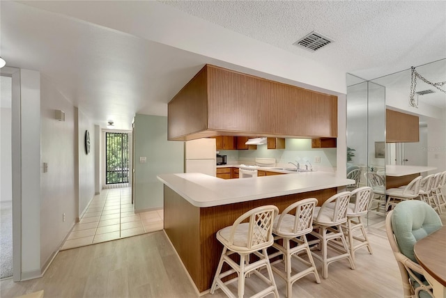 kitchen featuring light wood-type flooring, white appliances, kitchen peninsula, and a kitchen bar