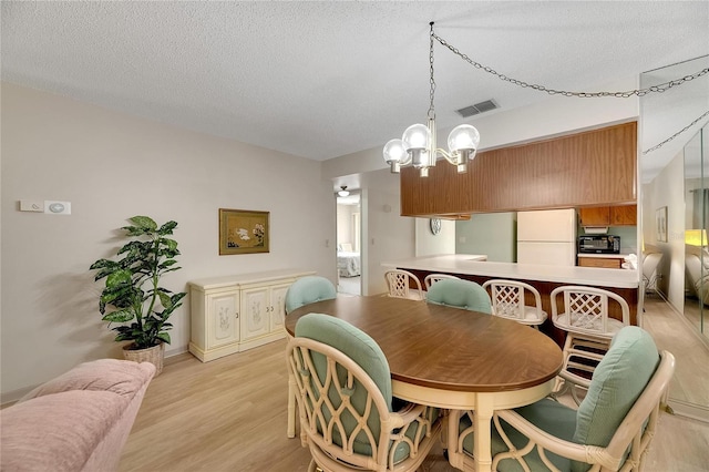 dining area with a notable chandelier, a textured ceiling, and light hardwood / wood-style floors