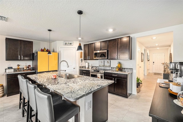 kitchen featuring pendant lighting, light stone counters, sink, stainless steel appliances, and a center island with sink