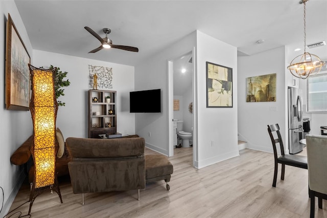 living room featuring ceiling fan with notable chandelier and light hardwood / wood-style flooring