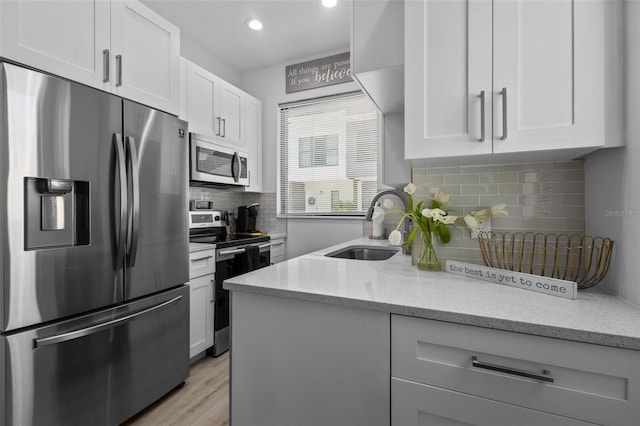 kitchen with white cabinetry, light stone countertops, stainless steel appliances, light hardwood / wood-style flooring, and sink