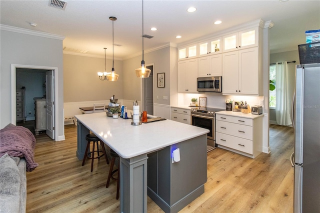 kitchen featuring white cabinets, an island with sink, ornamental molding, light hardwood / wood-style flooring, and appliances with stainless steel finishes