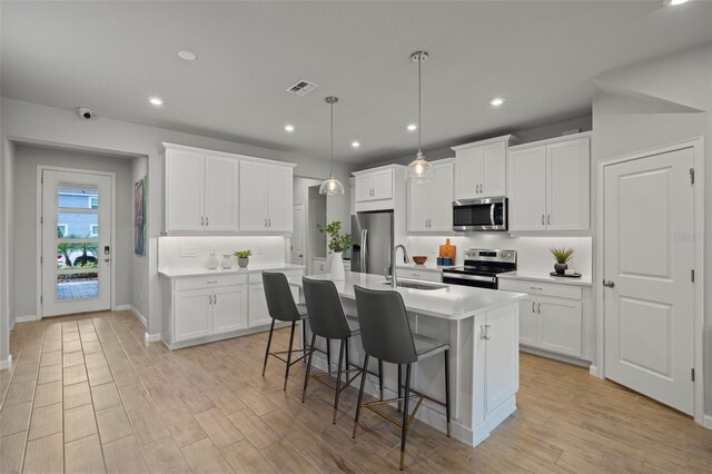 kitchen with stainless steel appliances, white cabinetry, and an island with sink