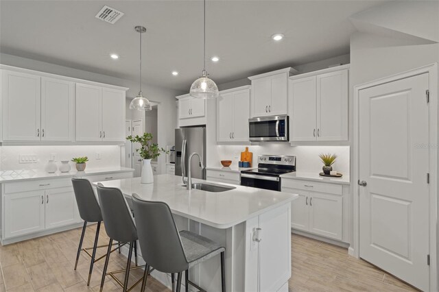 kitchen with pendant lighting, sink, an island with sink, white cabinetry, and stainless steel appliances